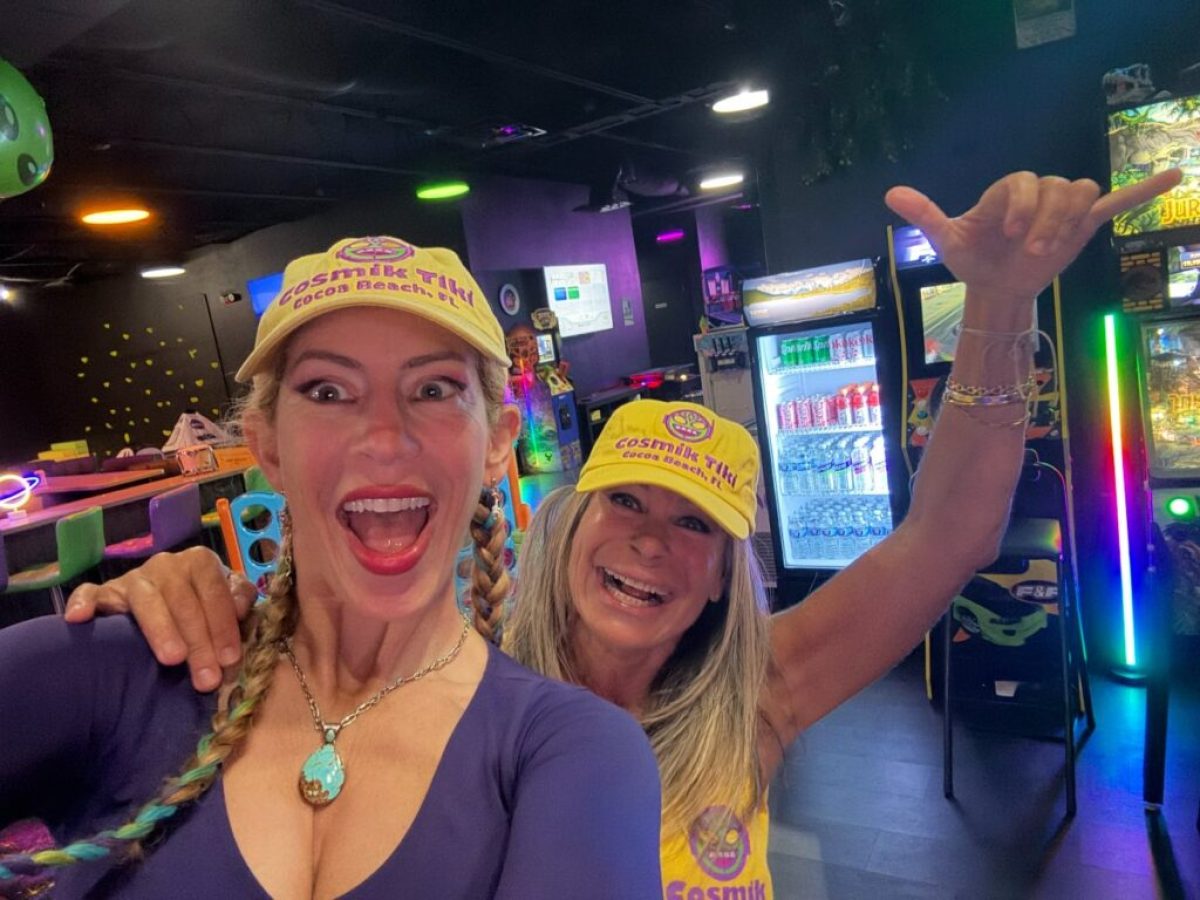 Two women in hats smiling excitedly in an arcade with colorful lights and games.