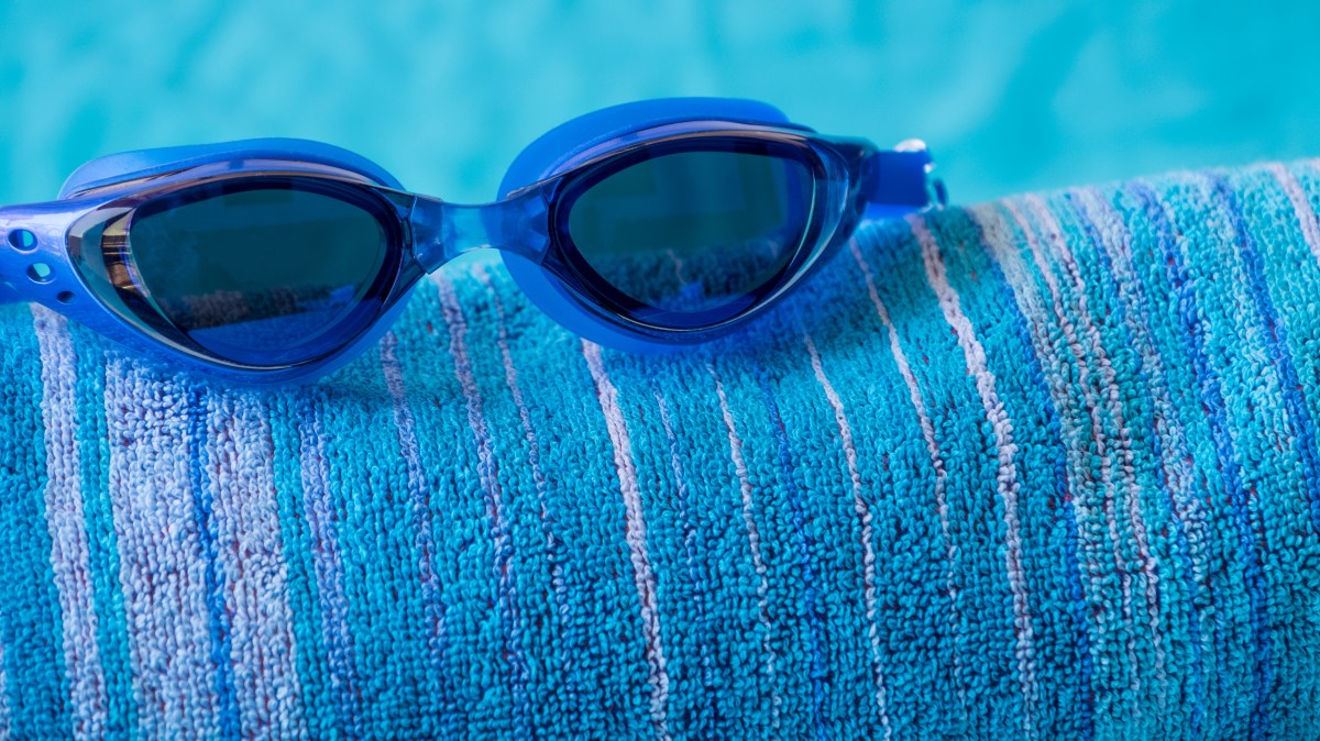 Blue swimming goggles on a rolled blue striped towel by the poolside.