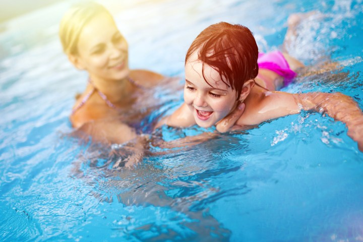 Smiling woman and child playing in a swimming pool on a sunny day.