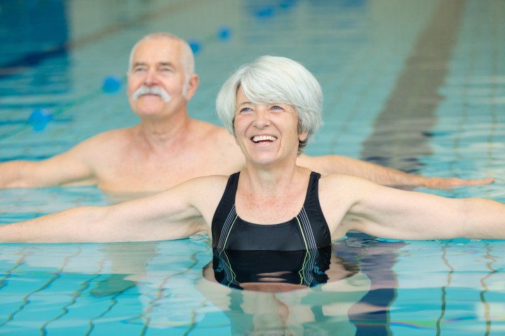 Two smiling older adults doing aqua aerobics in a swimming pool.