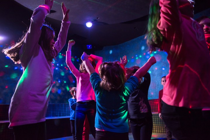Children dancing under colorful disco lights in a dark room.
