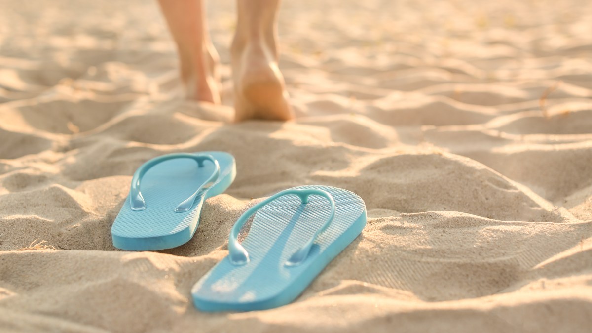 Blue flip-flops on sandy beach with bare feet walking away.