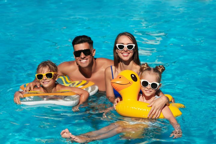 Family of four wearing sunglasses, enjoying a pool, with two kids on floaties.