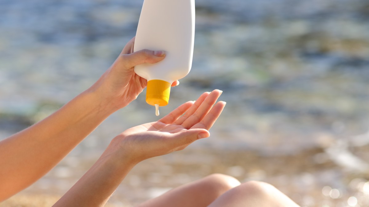 Person applying sunscreen on hands at the beach.