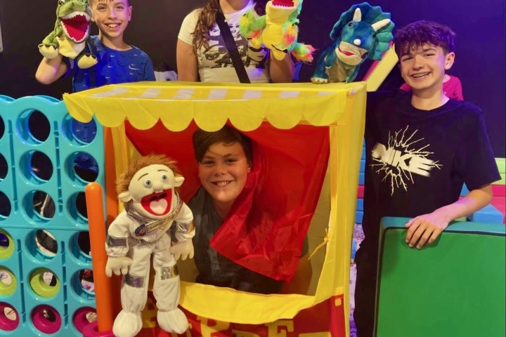 Four kids with puppet show booth, holding colorful hand puppets.