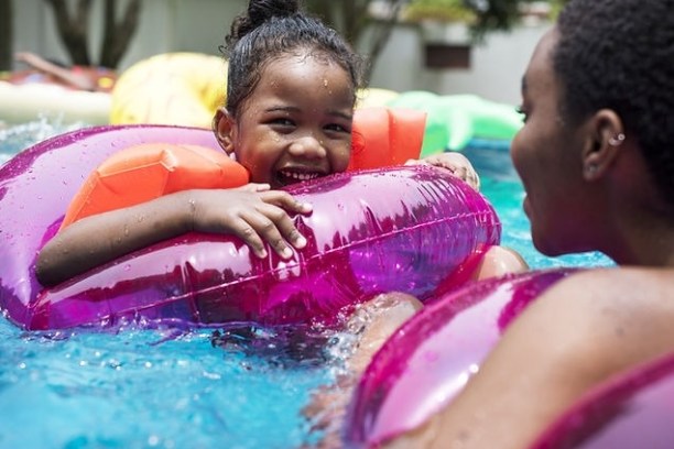 Child in a pink inflatable ring smiling with an adult in a pool.