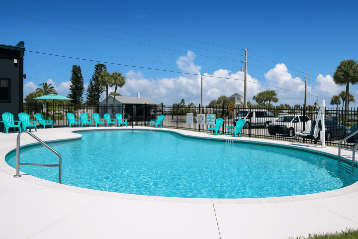 Outdoor pool with turquoise chairs, fenced area, and clear blue sky in the background.