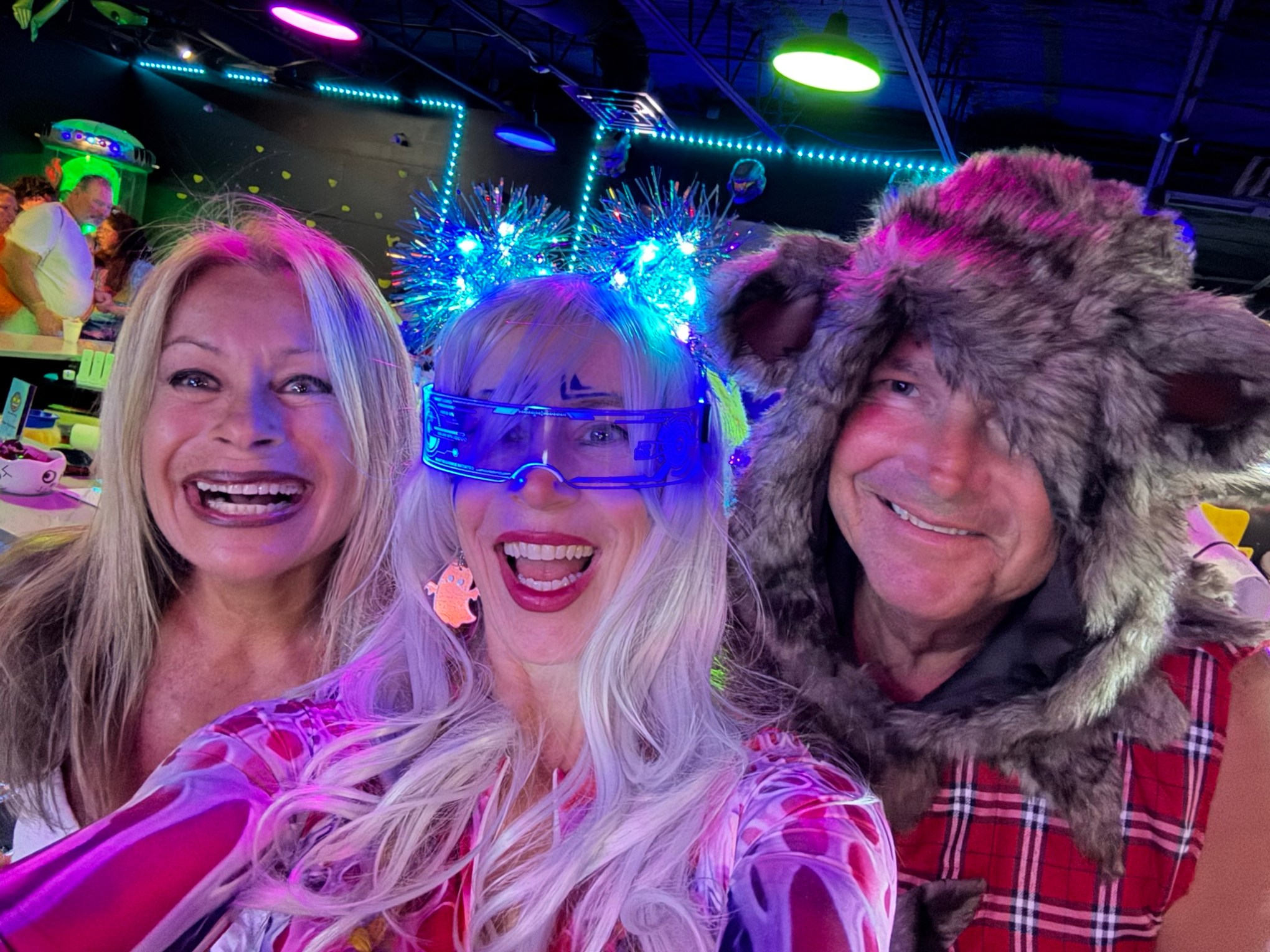 Three people in fun costumes smiling with colorful lights.