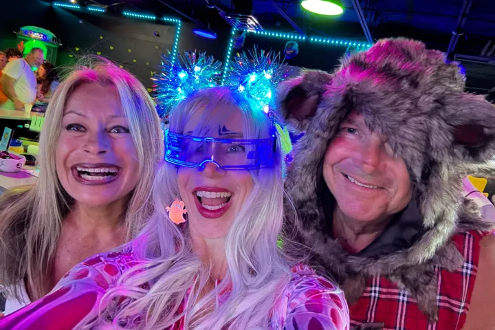 Three people in fun costumes smiling with colorful lights.