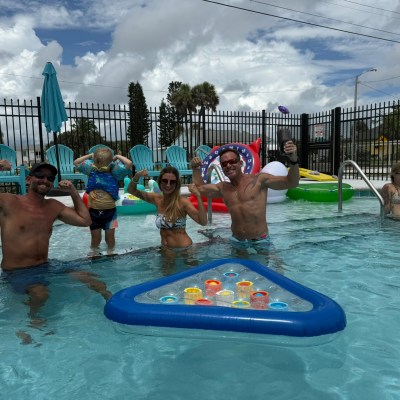 People in a pool enjoying a sunny day with floating toys and drinks.