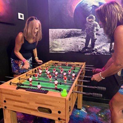 Two women playing foosball with an astronaut poster in the background.