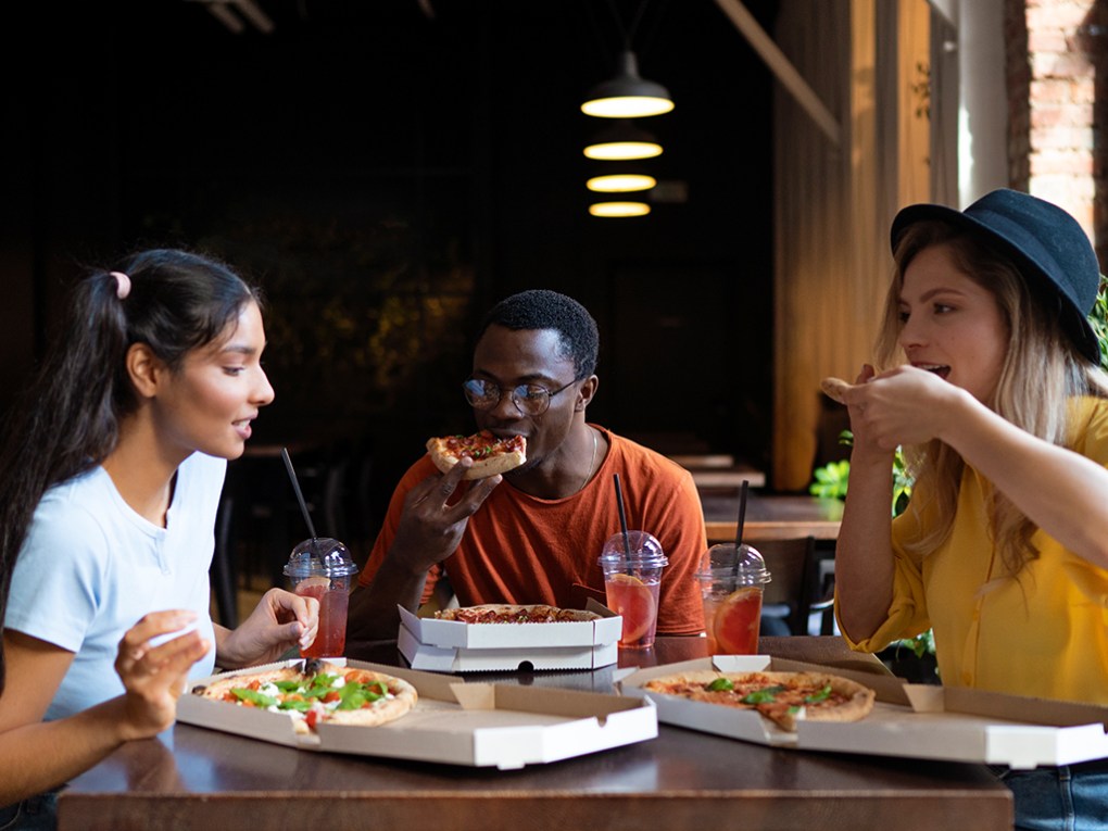 Pizza Three people enjoying pizza and drinks at a table in a cozy setting.