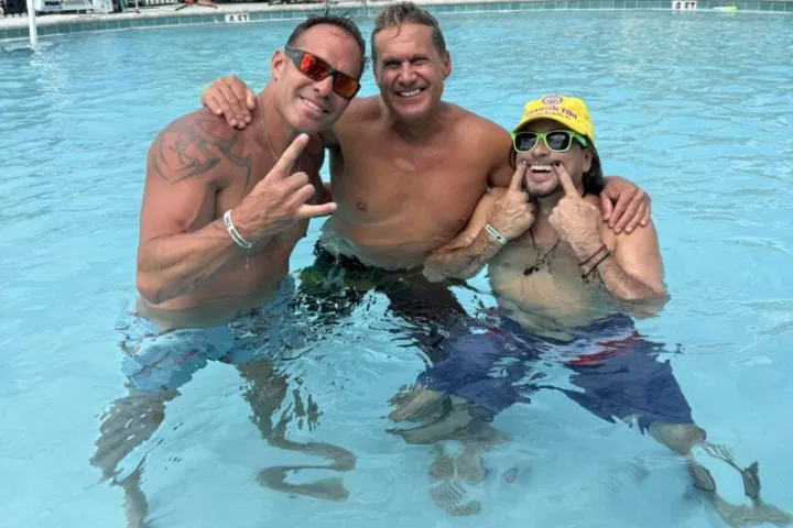 Three men smiling and posing in a swimming pool.