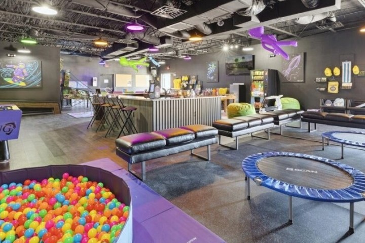 Indoor recreational area with ball pit, trampolines, lounge seating, and bright decor.