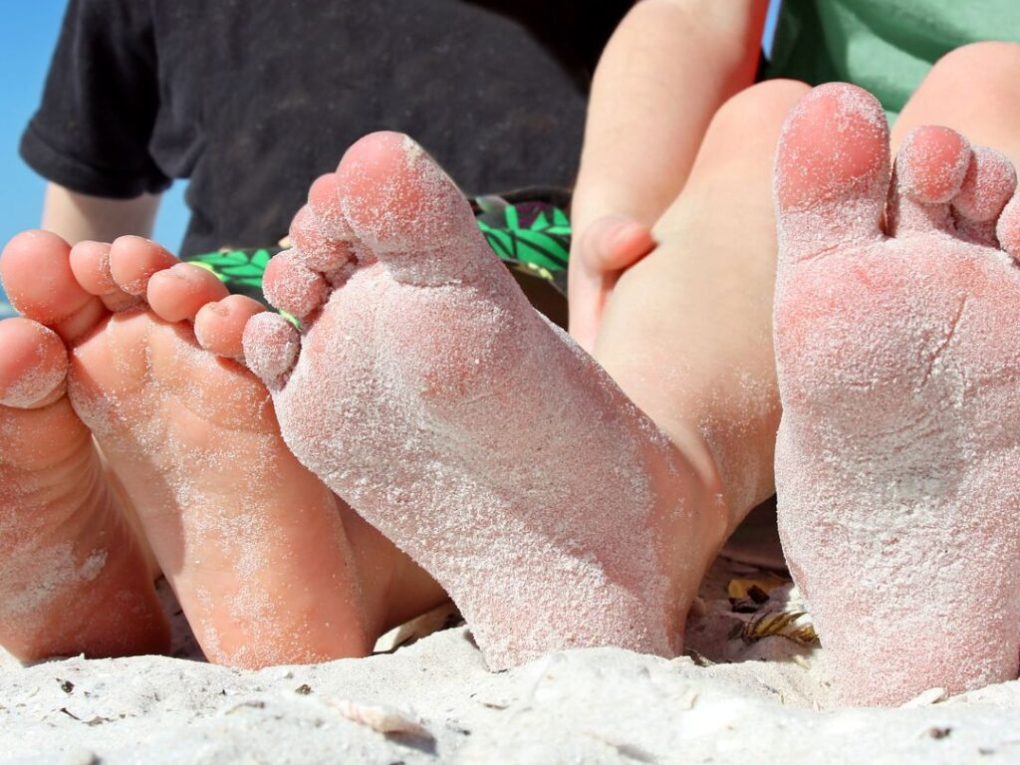 Where-Brevard-Comes-to-Play-27-1024×1024 Two children sitting on a beach, with sandy feet in the foreground.