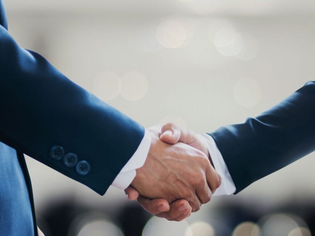 Two people in suits shaking hands in a professional setting.