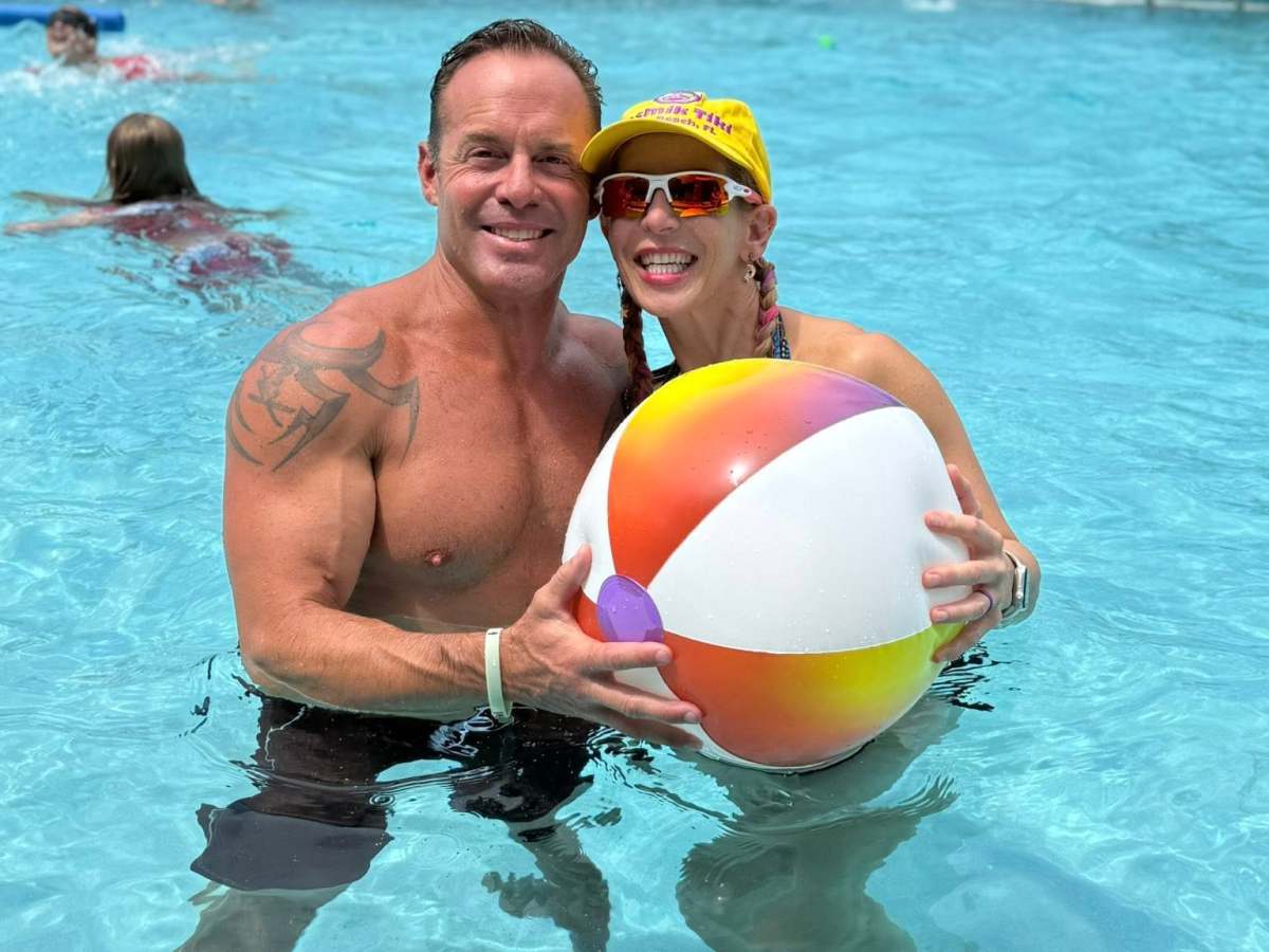 Two people in a pool holding a beach ball, smiling, sunny day.