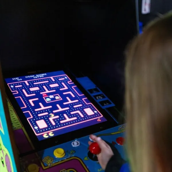 Person playing Ms. Pac-Man arcade game with joystick and buttons.