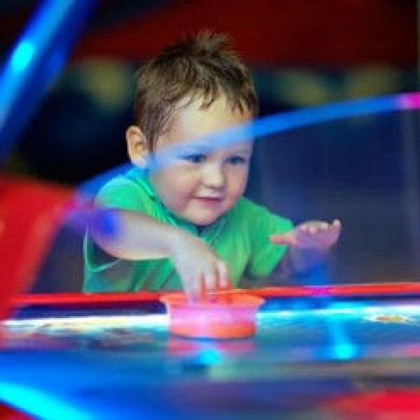 Child in green shirt playing air hockey with bright lights.