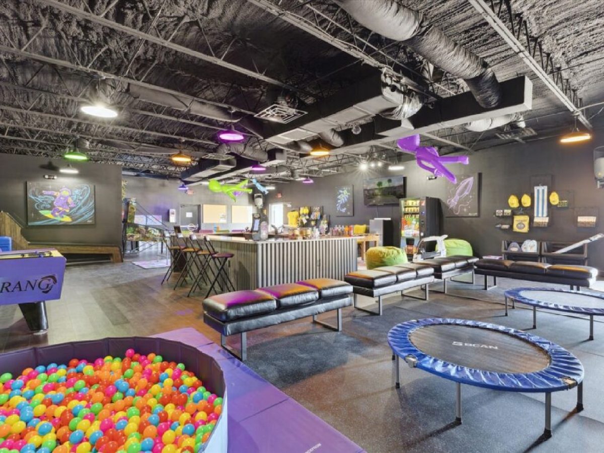 Indoor play area with ball pit, trampolines, colorful lights, seating, and wall decorations in a modern space.