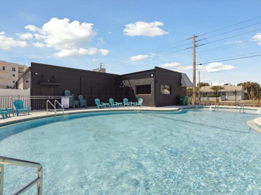 Outdoor pool with turquoise chairs, black building, and clear sky.