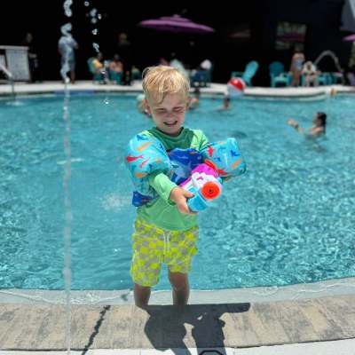 Child in floaties holding toy gun by pool with depth marker '4 FT. NO DIVING'.
